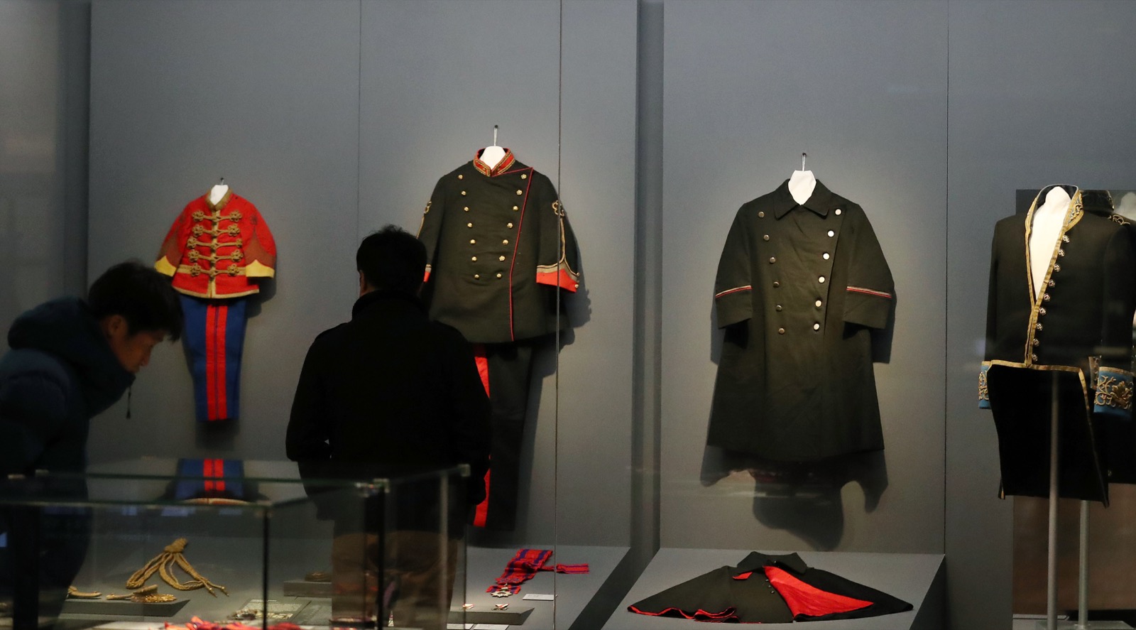 国立古宮博物館の展示室で、来場者が大韓帝国の王室の軍服・礼服のケースを見ている実際の展示空間の写真です。