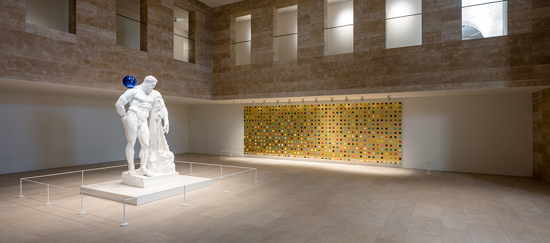 パラダイスシティ・アートスペースの展示室 — ダミアン・ハーストの白いヘラクレス彫刻とカラードットの絵画が並ぶ実際の空間。